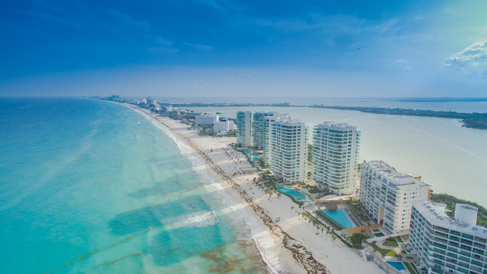 Luftfoto af Cancuns hotelzone med hvid sandstrand, turkisblåt hav og en række høje hoteller langs Boulevard Kukulcán med Nichupté-lagunen bagved