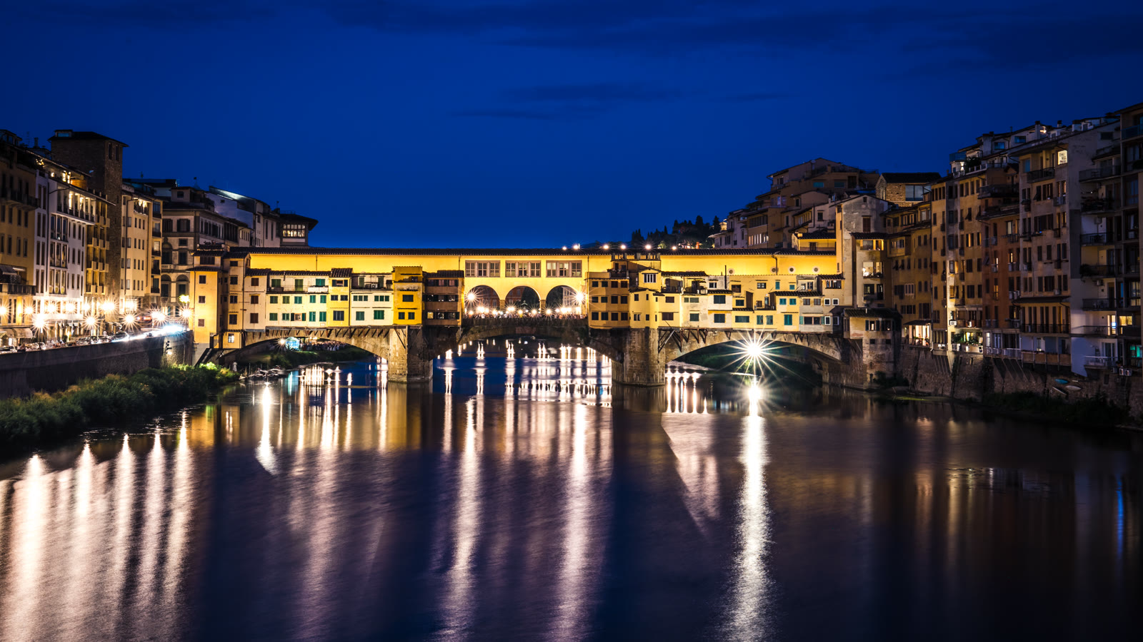Ponte Vecchio i Firenze oplyst om aftenen med spejling i Arno-floden