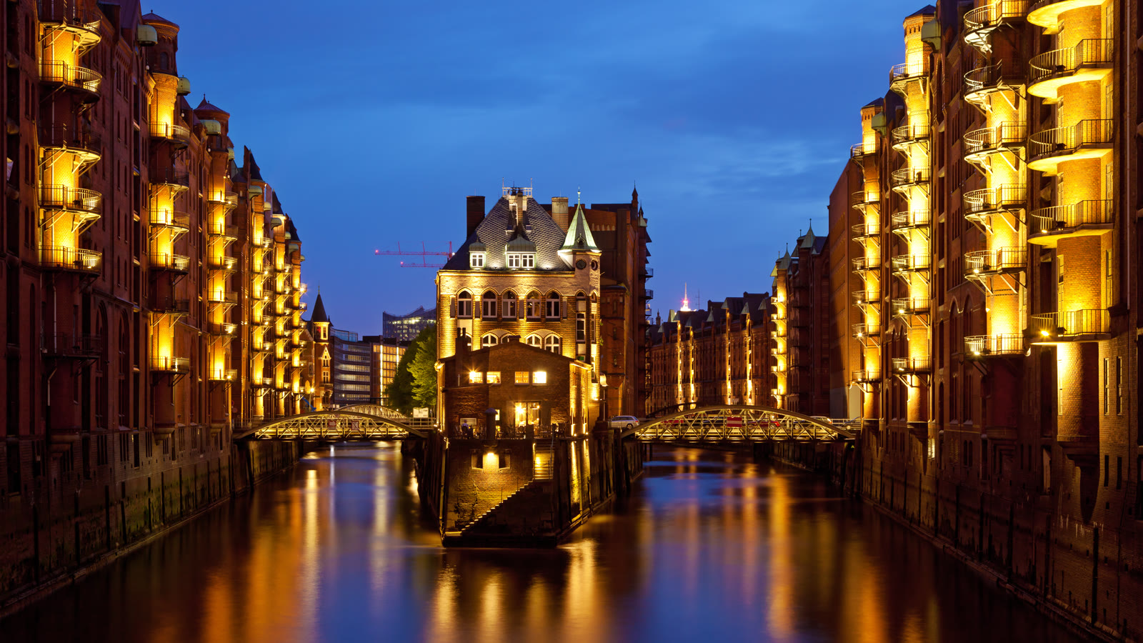 Speicherstadt om aftenen med det oplyste Wasserschloss mellem to kanaler, røde pakhuse og buede jernbroer