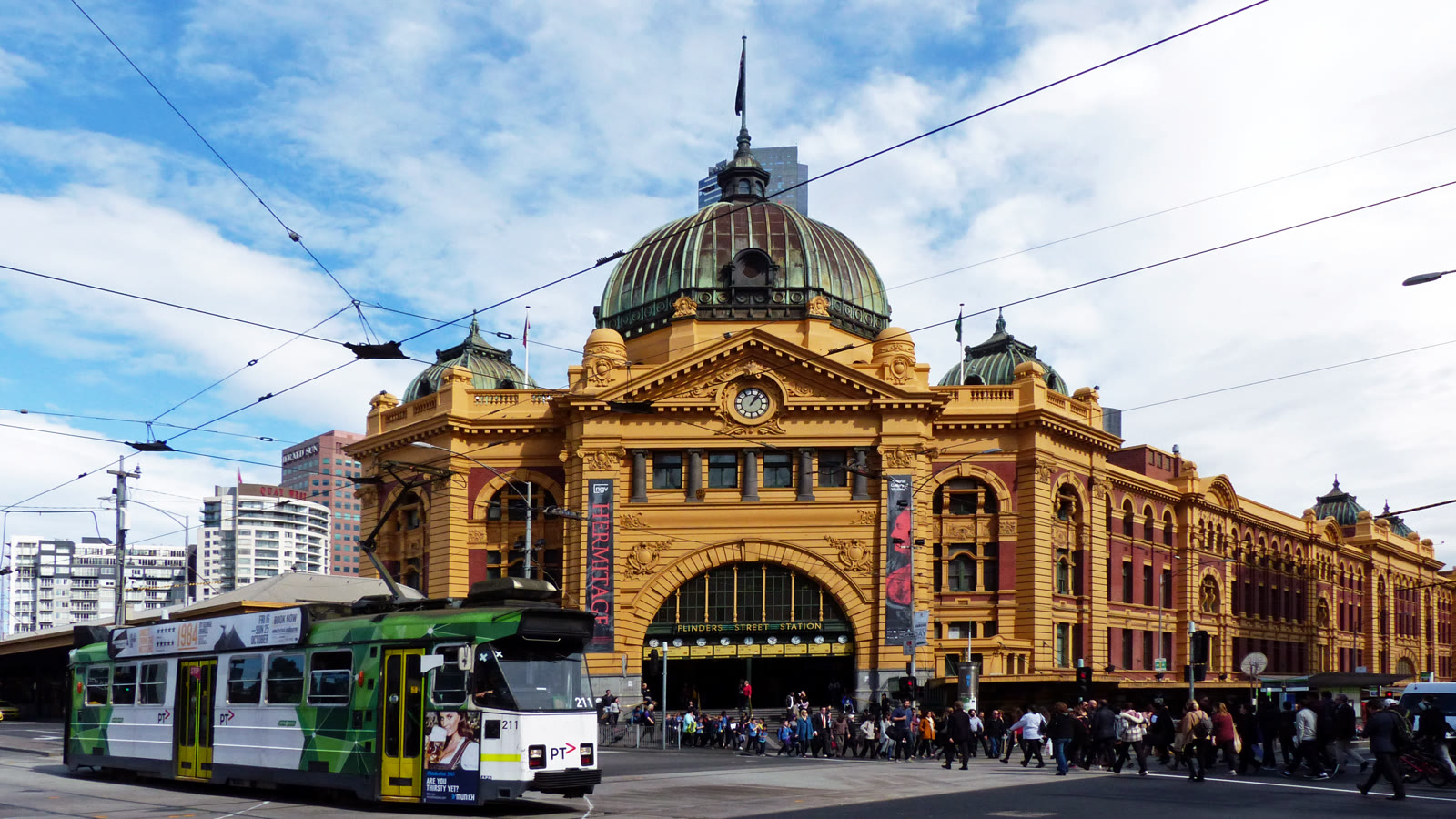 Flinders Street Station i Melbourne med okkergul facade, grøn kobberkuppel og en sporvogn foran hovedindgangen