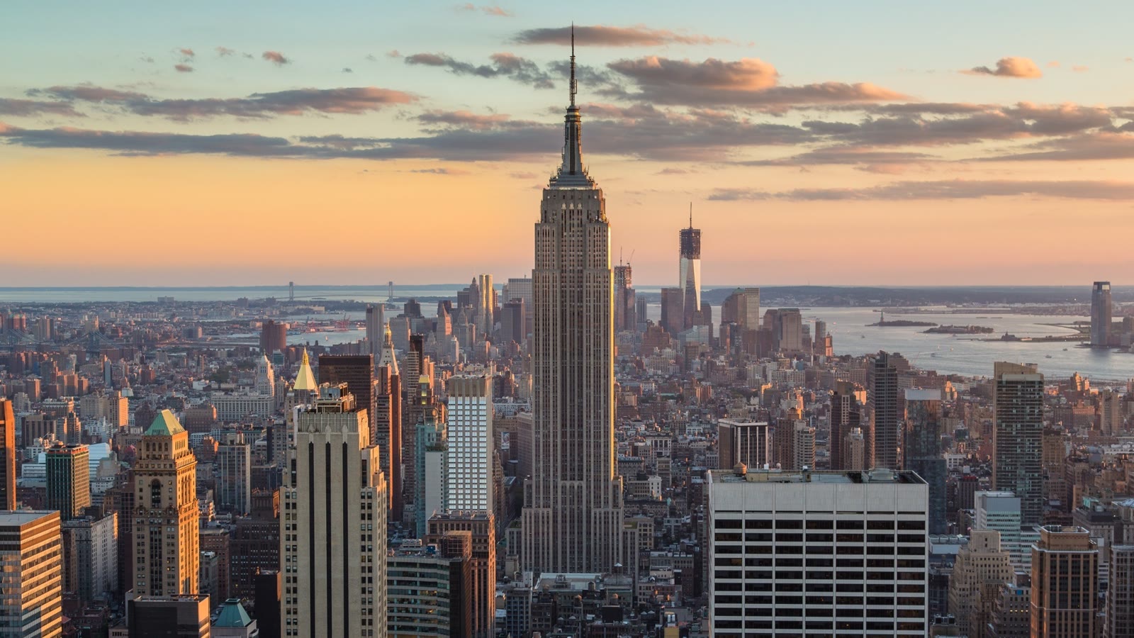 Empire State Building rager op over Midtown Manhattan i aftensol, med New Yorks havn i baggrunden