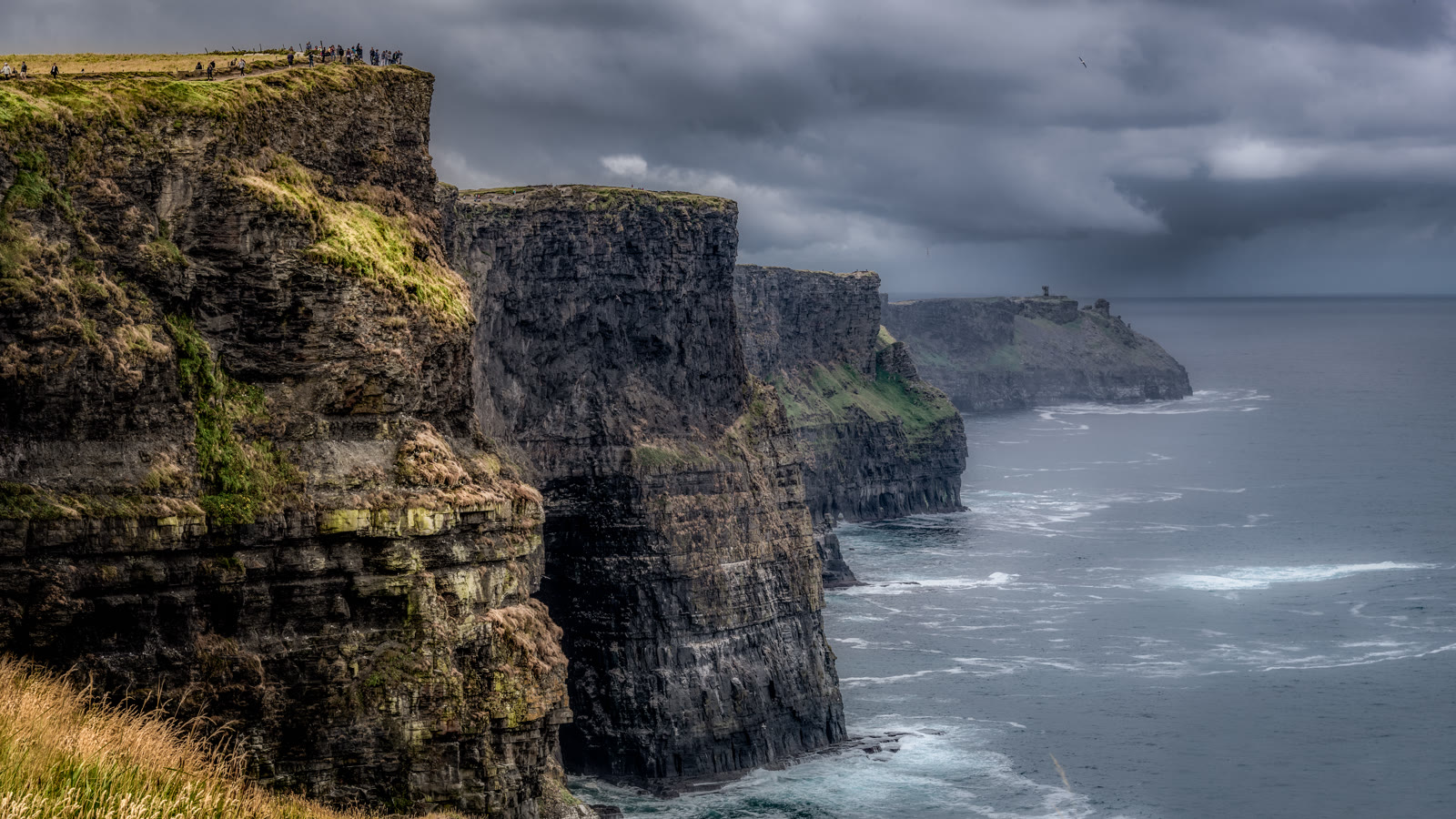 Cliffs of Moher med lodrette klippevægge ud mod Atlanterhavet under en mørk, regntung himmel