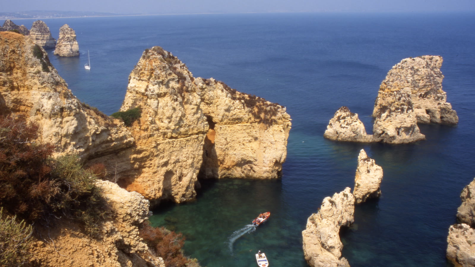 Gyldne klipper og klippesøjler i turkist vand ved Ponta da Piedade nær Lagos på Algarve-kysten med to små både